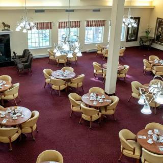 A spacious dining room with multiple round tables and chairs arranged on a red carpeted floor.