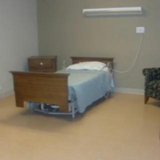 An empty hospital room with a single bed and nightstand.