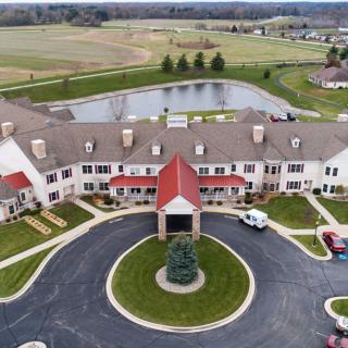 Aerial view of a large residential building with a circular driveway and a pond in the background.