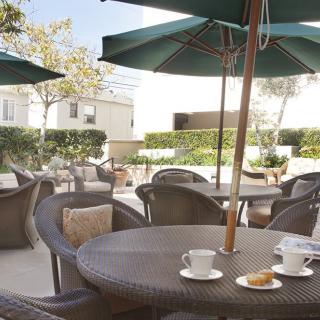 A cozy outdoor patio with rattan chairs and tables, featuring coffee cups under large umbrellas on a sunny day.
