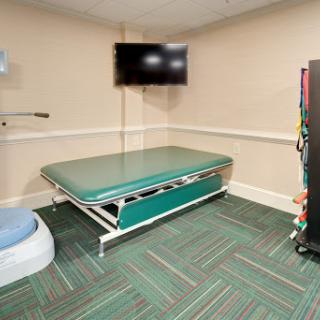A therapy room equipped with a treatment table, television, and various rehabilitation tools.