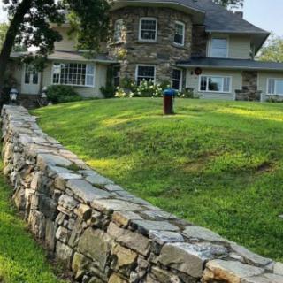A large stone house with a surrounding stone wall and well-maintained lawn.