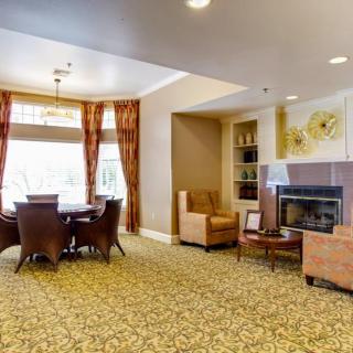A cozy living room with a fireplace, comfortable chairs, and a dining table near large windows.