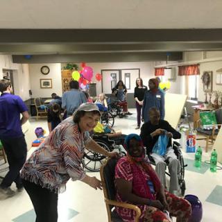 A lively celebration at a senior center, featuring residents engaging with staff and each other amidst colorful decorations.