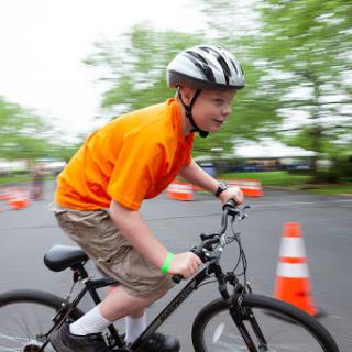 A child riding a bicycle wearing a helmet, navigating through cones in an outdoor setting.
