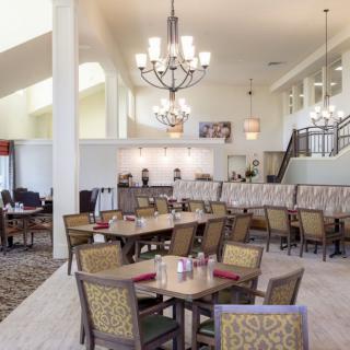 A spacious and elegantly decorated dining area with multiple tables and chairs, featuring chandeliers hanging from the high ceiling.