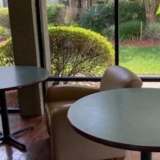 A cozy seating area with round tables and chairs next to a large window overlooking a garden.