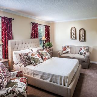 A cozy bedroom featuring a bed with decorative pillows, a small couch, and elegant curtains.