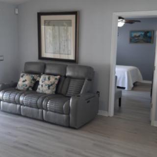 A modern living room with a gray leather sofa and a view into an adjacent bedroom.