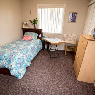 A cozy bedroom with a single bed, window, and basic furniture.