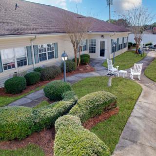 A well-maintained garden with a pathway leading to a building, featuring neatly trimmed bushes and outdoor seating.