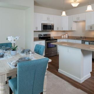 A modern kitchen with an adjacent dining area featuring white cabinets, stainless steel appliances, and blue upholstered chairs.