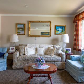 A cozy living room with a sofa, armchairs, and a coffee table, elegantly decorated with paintings and lamps.