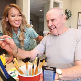 A nurse assists an elderly man during a painting session.