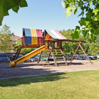 A colorful playground with a slide and swing set on a sunny day, surrounded by trees and grass.