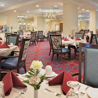 A spacious, elegantly decorated dining area with neatly arranged tables and chairs, featuring chandeliers and floral centerpieces.