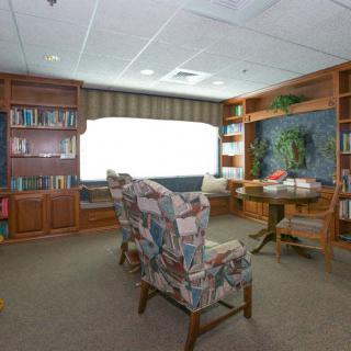 A cozy library reading area with bookshelves, comfortable chairs, and a large window.