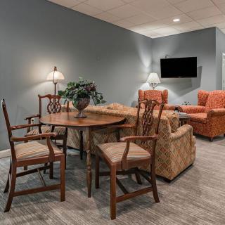 A cozy living room with a round wooden table, cushioned chairs, and a wall-mounted TV.