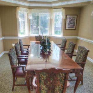 A well-lit dining room with a large wooden table and upholstered chairs.
