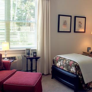 A cozy bedroom with a single bed, artwork on the wall, and a comfortable chair by the window.