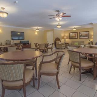 A spacious dining area with multiple tables and chairs, featuring ceiling fans and soft lighting.