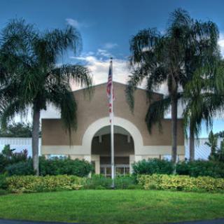 A beautifully designed building surrounded by palm trees, featuring a flag at the entrance.
