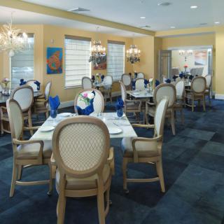 An elegant dining area with neatly arranged tables and chairs, adorned with blue accents and lit by chandeliers.