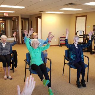A group of seniors participating in a chair exercise class indoors.