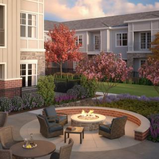 A cozy outdoor courtyard with a fire pit and seating area surrounded by landscaped greenery.