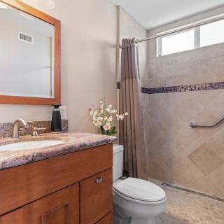 A modern bathroom featuring a shower with a tiled wall, a sink with a marble countertop, and decorative flowers on the vanity.