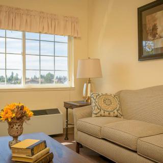A cozy living room with a comfortable sofa, a lamp on a side table, and a window letting in natural light.