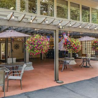 An inviting outdoor patio with tables, chairs, umbrellas, and vibrant hanging floral arrangements.