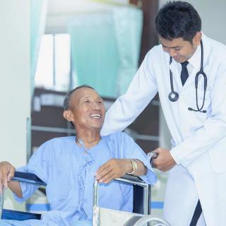 A doctor interacting with a smiling patient in a wheelchair.