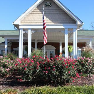 A well-landscaped entrance of a building with a flag and vibrant flower garden.