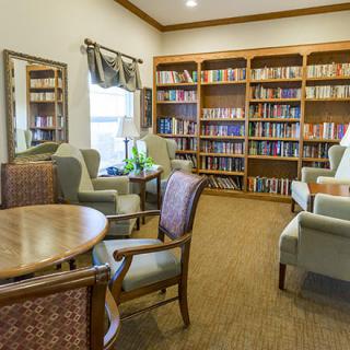 A cozy library room with bookshelves, comfortable chairs, and tables.