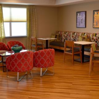 A cozy seating area with red chairs and wooden flooring, featuring tables and wall decorations.