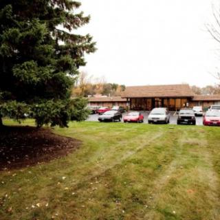 A small parking lot with several cars in front of a building surrounded by grass and trees.