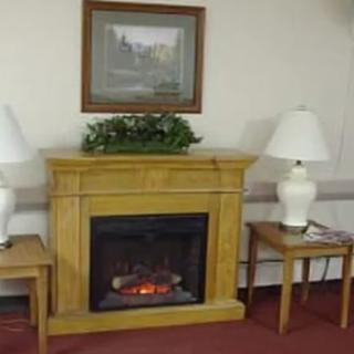 A cozy living room setup featuring a wooden fireplace with a framed picture and greenery on top, flanked by two lamps on side tables.