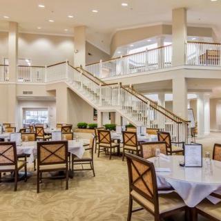 A spacious and elegant dining area with neatly arranged tables and chairs, featuring a large staircase.