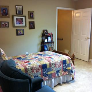 A cozy bedroom with a colorful quilt on the bed, armchair, and photographs on the wall.