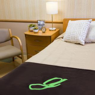 A cozy hospital room featuring a neatly made bed, a comfortable chair, and a table with personal items.