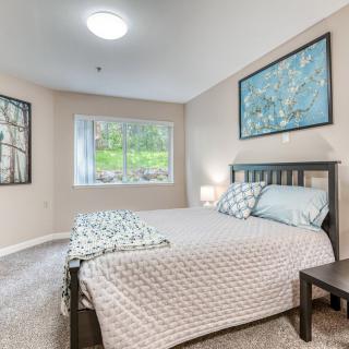 A cozy and well-decorated bedroom featuring a bed with patterned bedding, artwork on the walls, and a large window.