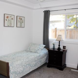 A cozy bedroom with a single bed, nightstand, and window adorned with curtains.