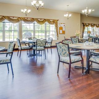 A spacious dining area with multiple tables and chairs, adorned with chandeliers and large windows with decorated curtains.