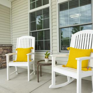A cozy porch with white rocking chairs and bright yellow pillows beside a small side table.