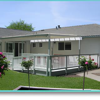 A backyard view of a house with a deck and covered patio, surrounded by a well-maintained lawn and garden.