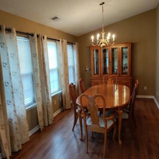 A spacious dining room with a wooden table, matching chairs, and a chandelier overhead.