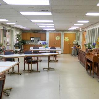 A community room with tables, chairs, and a kitchen area.