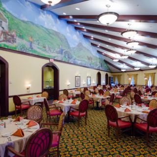 A spacious dining area featuring elegantly set tables, comfortable chairs, and a beautiful mural on the ceiling.