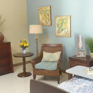 A cozy living room with retro-style furniture and decor, featuring a wooden chair, side table, lamp, and colorful wall art.